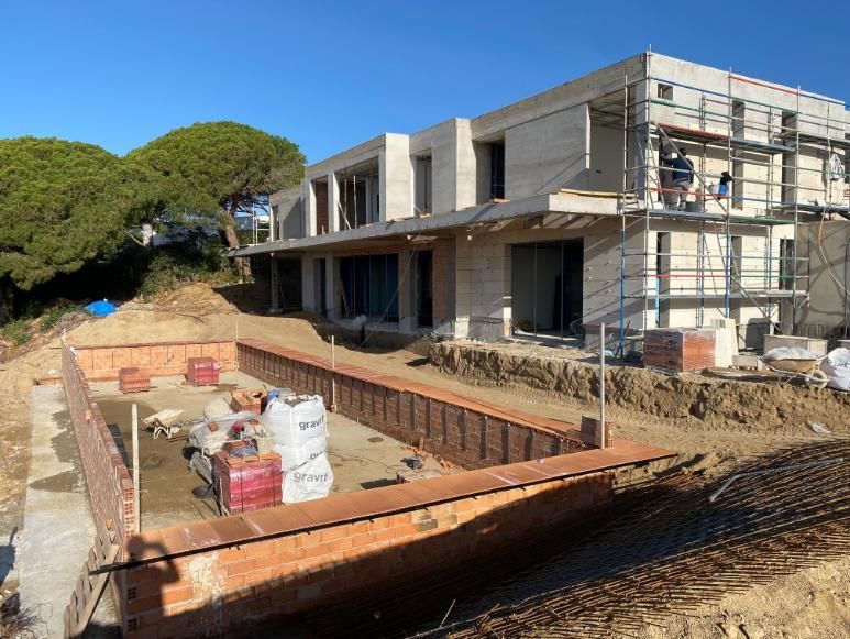 casa de dos pisos parcialmente construida con andamios, ladrillos y área excavada en un entorno soleado.