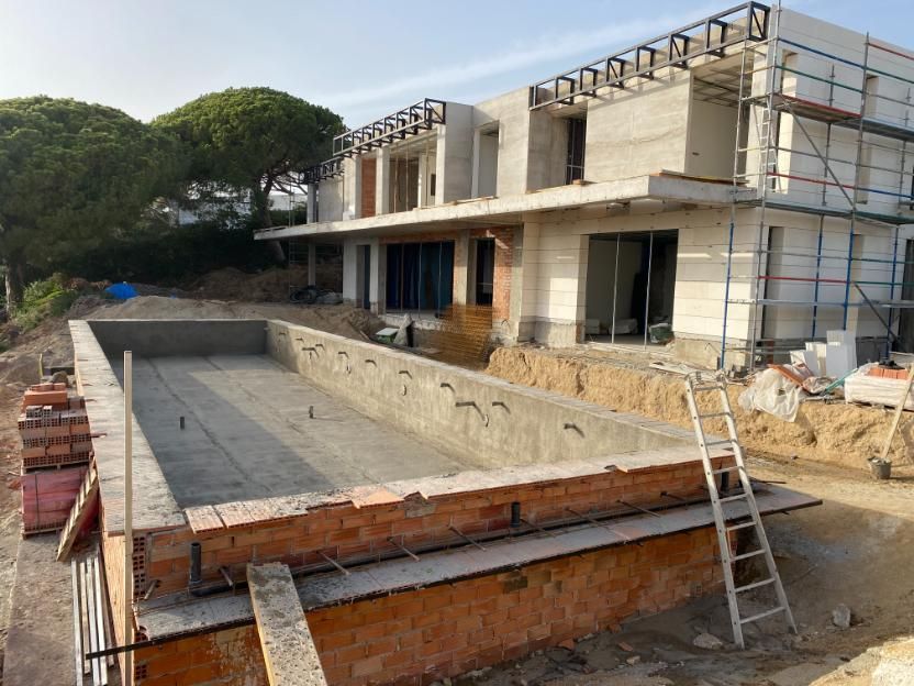 Terreno en construcción con piscina rectangular en frente de casa de dos plantas.