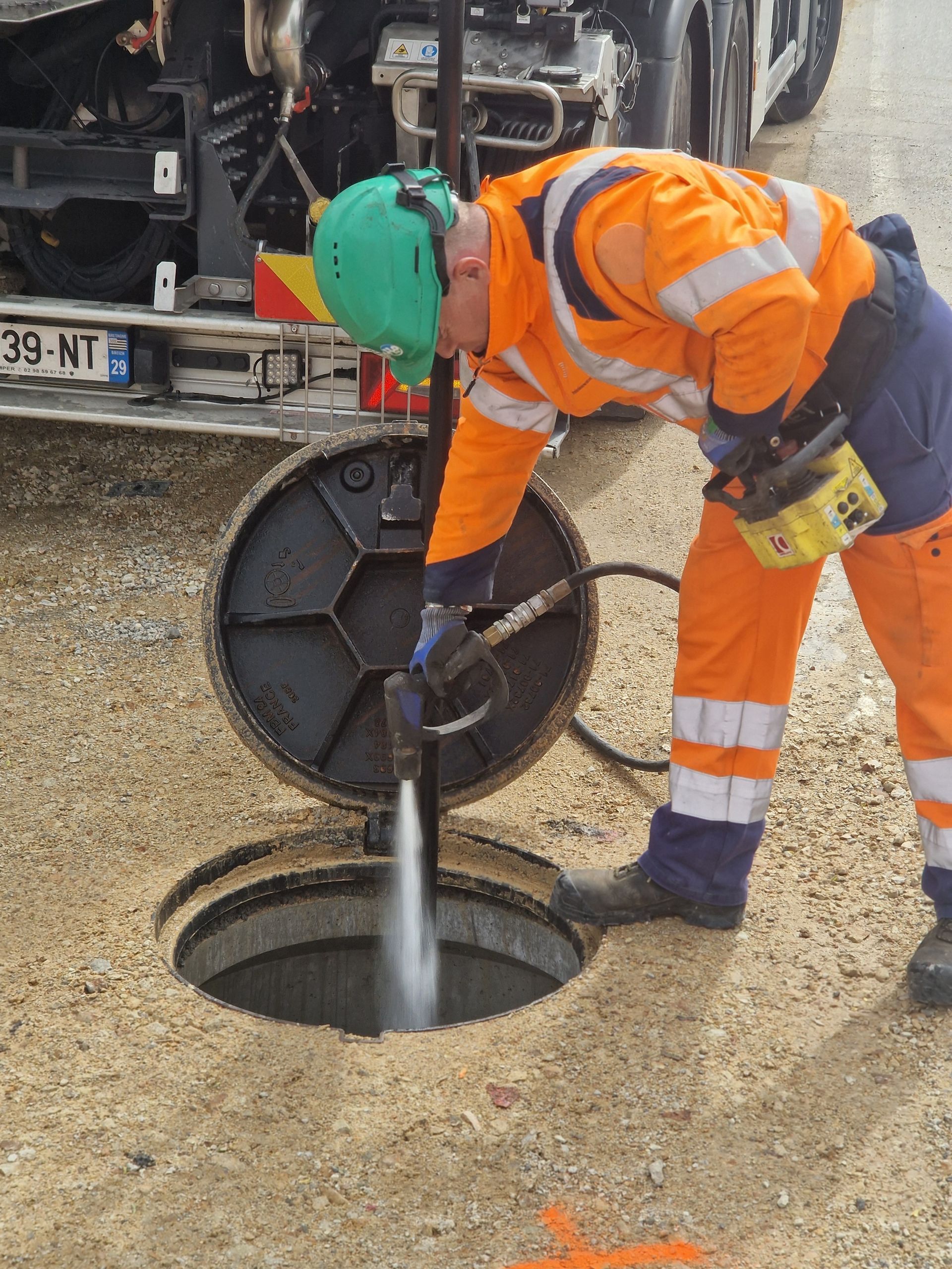 Un technicien avec un jet à haute pression dans une bouche d'égout.