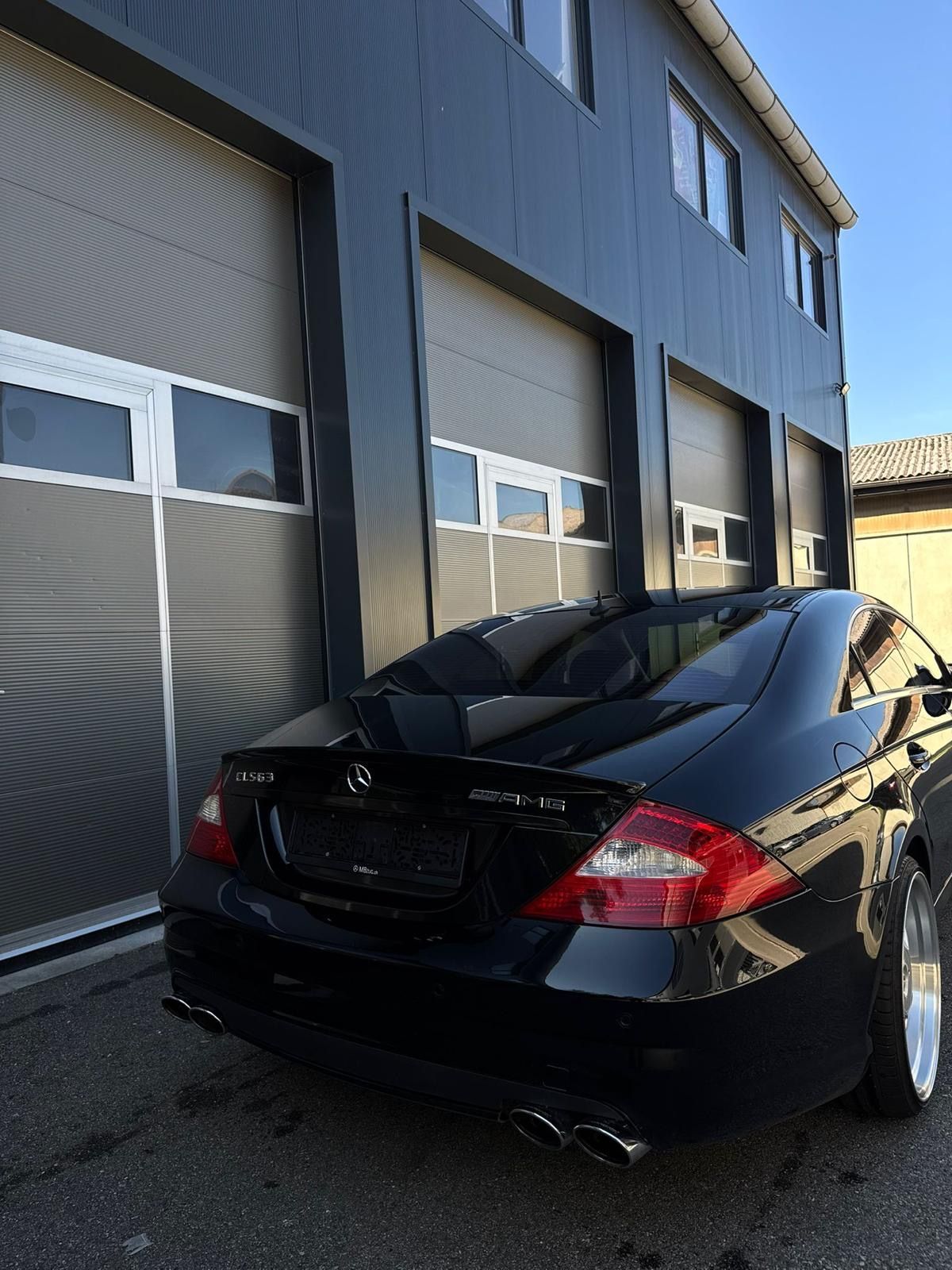 Schwarzer Mercedes-Benz parkt vor einem modernen grauen Gebäude mit Garagentoren.