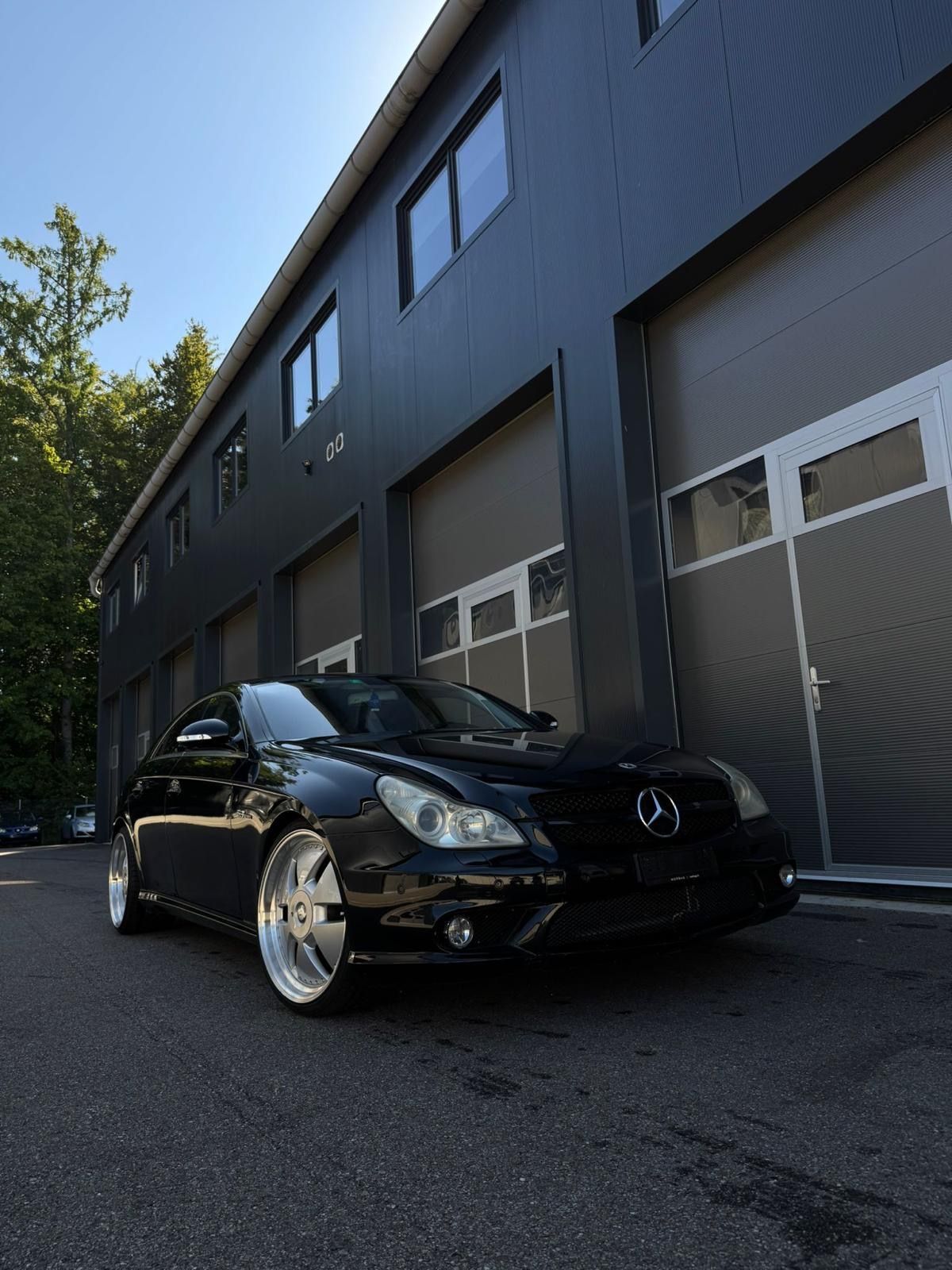 Schwarzer Mercedes-Benz parkt vor einem modernen grauen Gebäude mit geschlossenen Garagentoren, sonniger Tag.