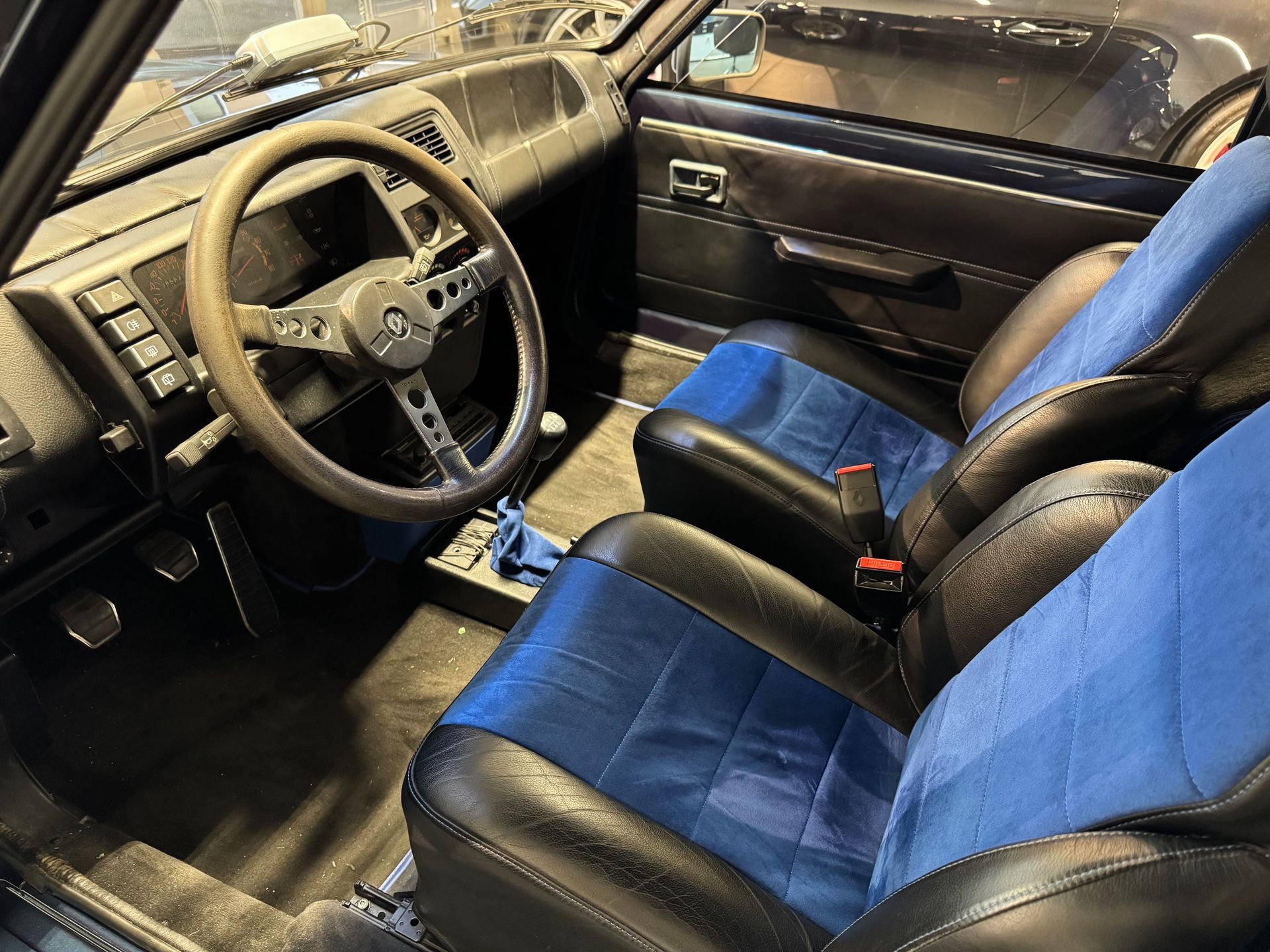 Innenraum eines Fahrzeugs mit schwarz-blauen Schalensitzen, einem Lenkrad und einem dunklen Armaturenbrett.