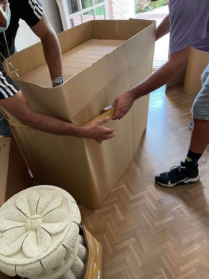 Dos hombres mueven una gran caja de cartón sobre un piso de madera.