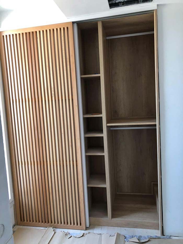 Un armario de madera con puertas correderas y estantes en una habitación.
