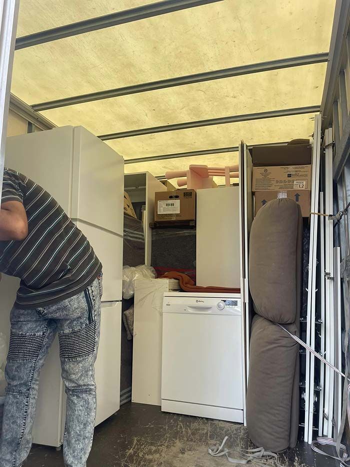 Un hombre está parado en la parte trasera de un camión lleno de electrodomésticos.