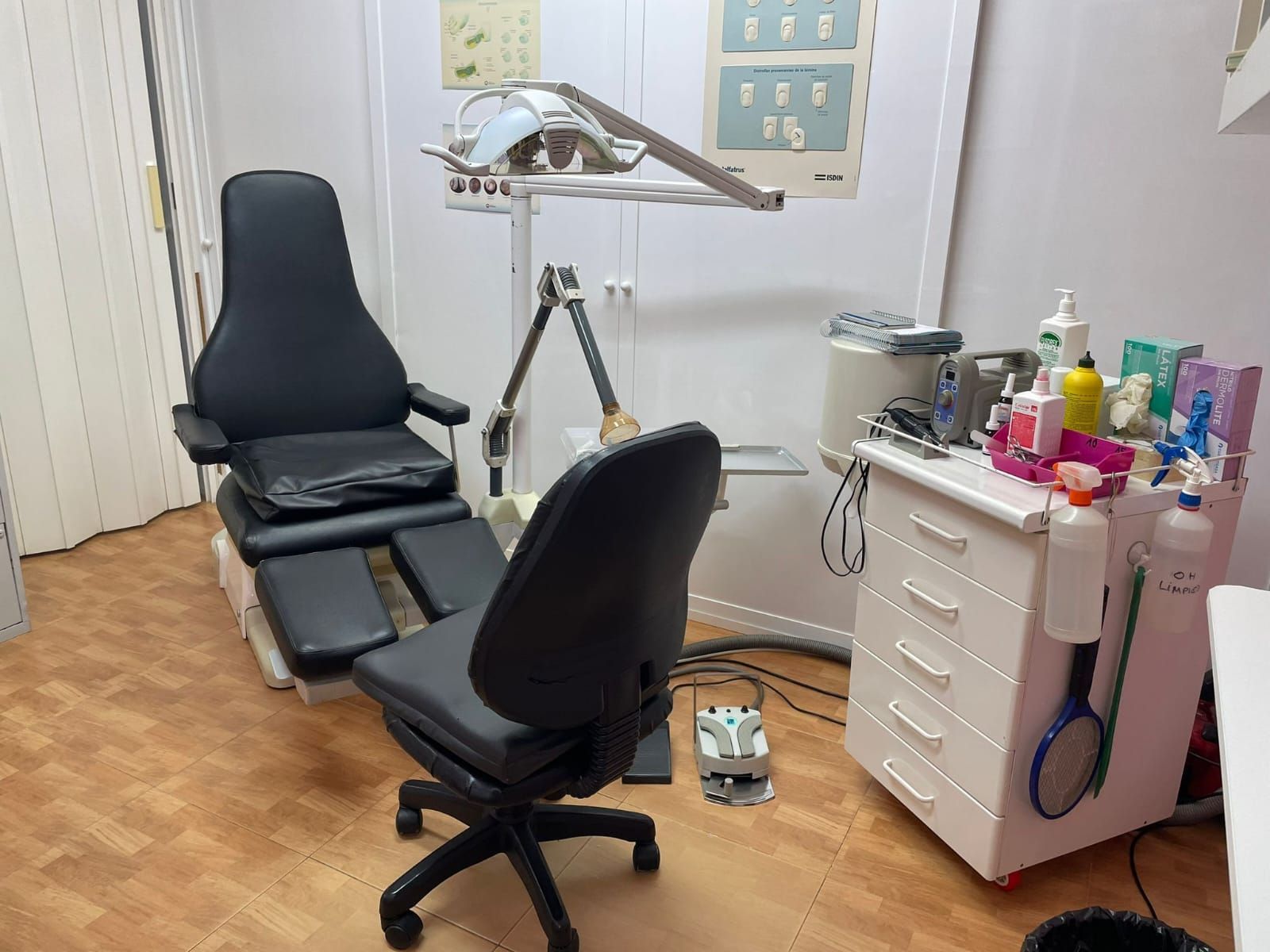 Consultorio de podología con silla negra, equipo y reposapiés. Luz brillante y gabinetes blancos.