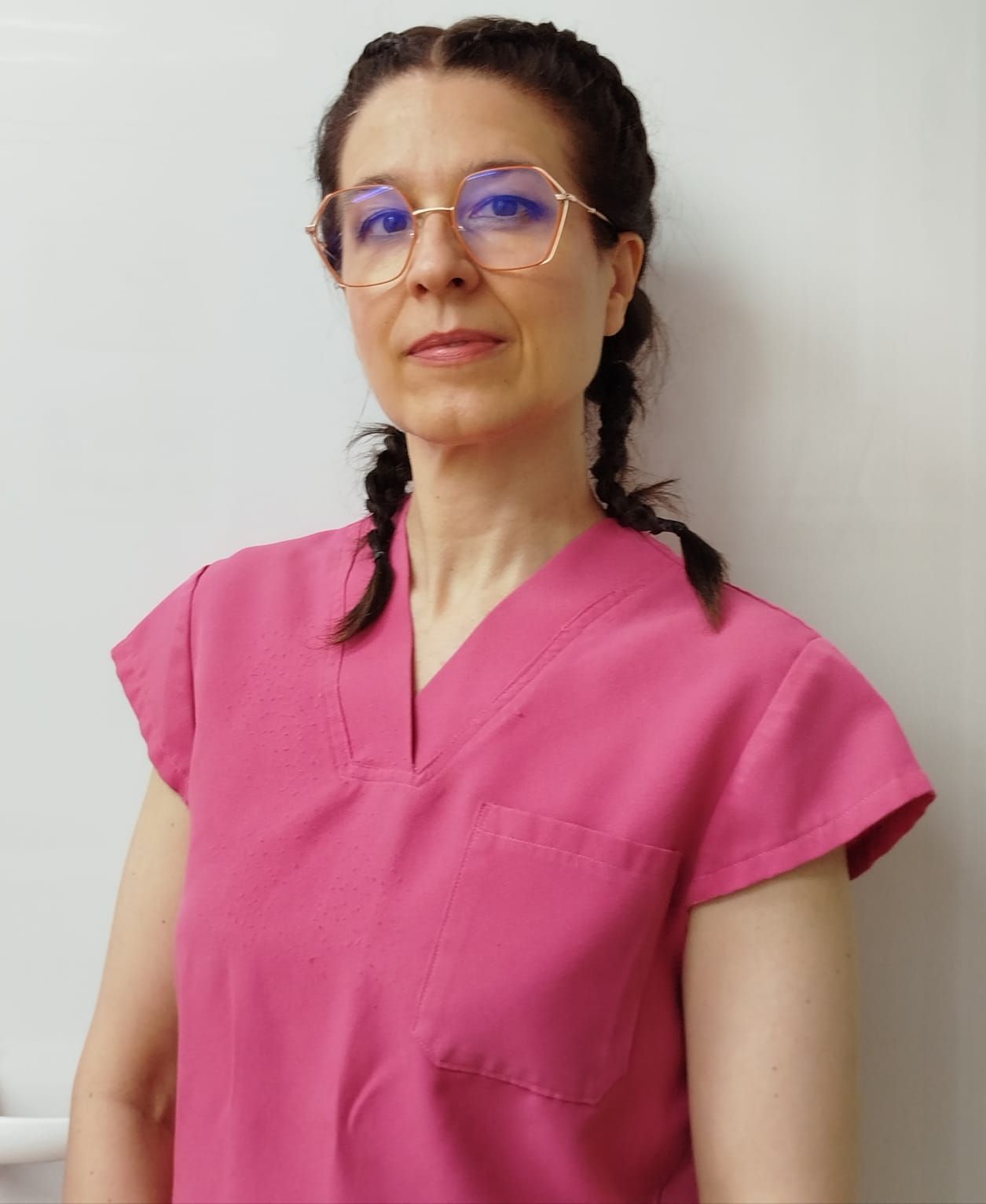 Mujer con uniforme rosa y gafas, con trenzas, mirando hacia el frente.