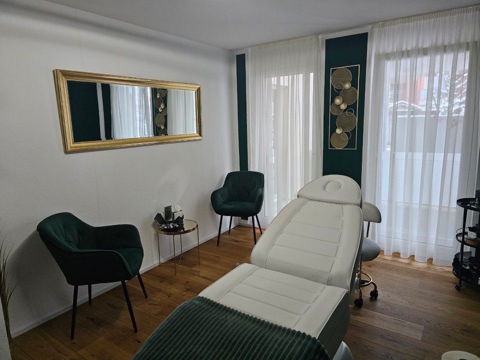 Kosmetikstudio: weisse Behandlungsliege, grüne Stühle, goldener Spiegel, grüne Akzentwand, helle Vorhänge.