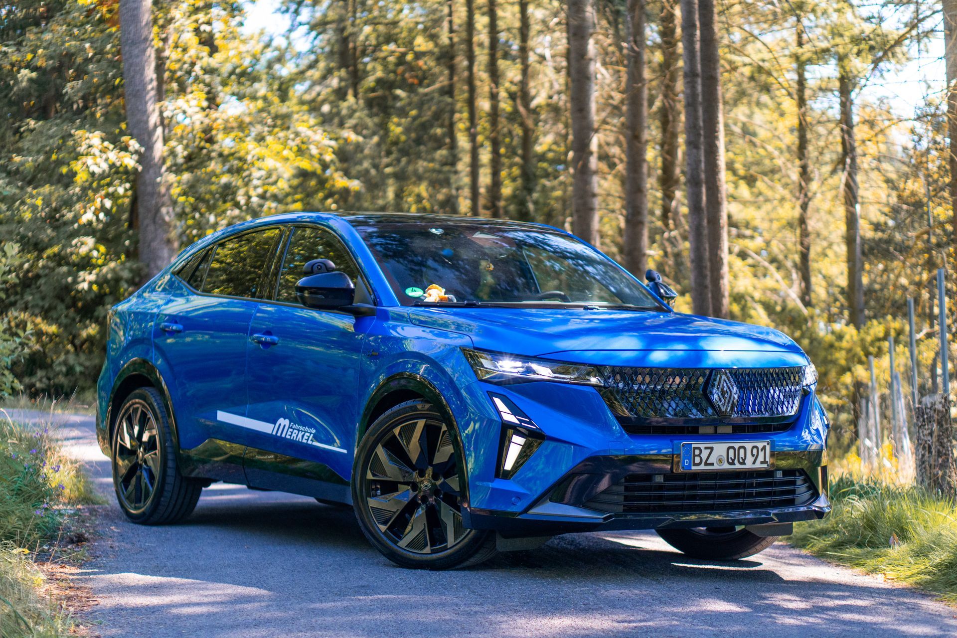 Blauer SUV, geparkt auf einer unbefestigten Straße in einer Waldlandschaft, schwarze Räder und Verkleidung.
