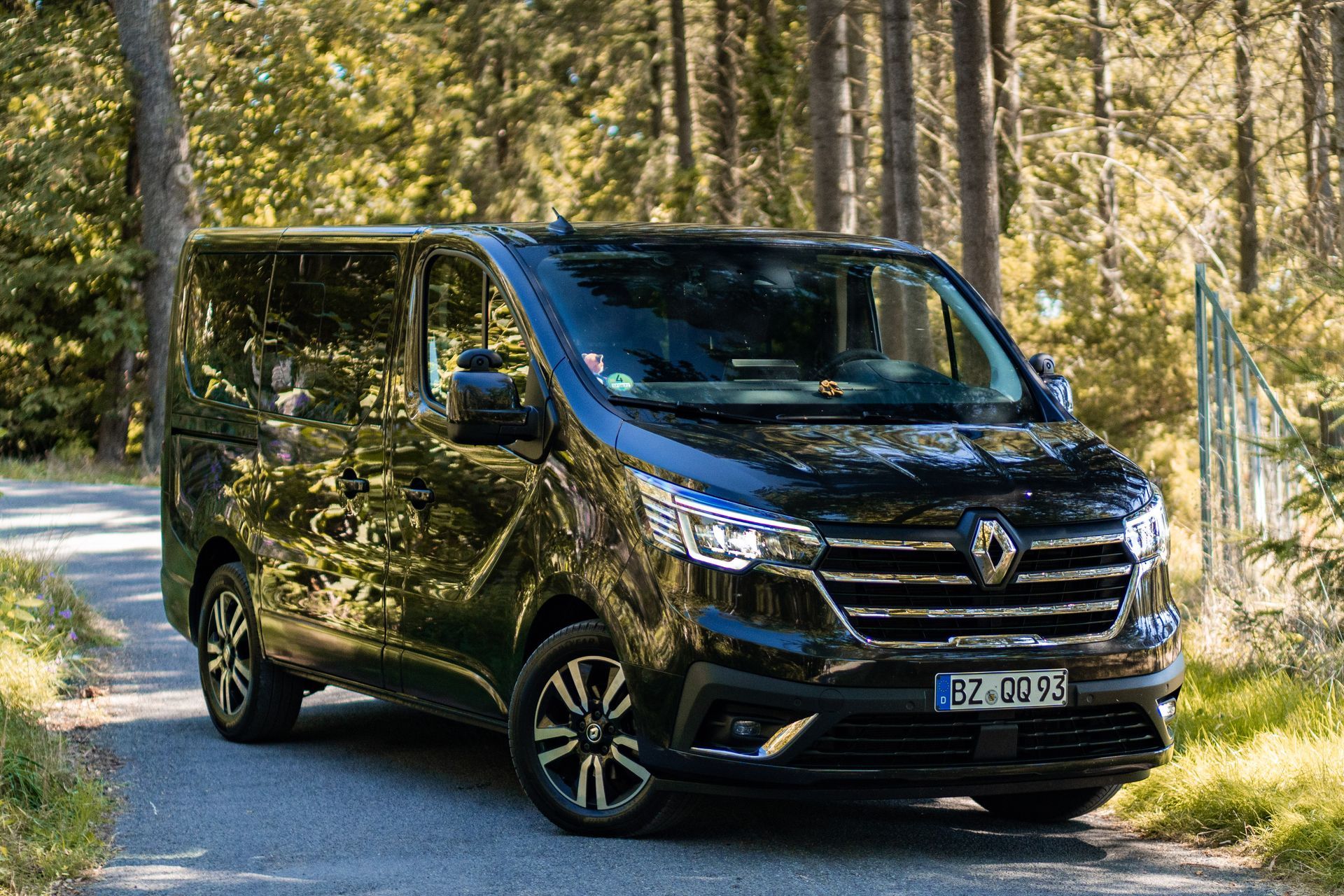 Schwarzer Renault Trafic-Transporter, geparkt auf einer asphaltierten Straße in einer Waldlandschaft.