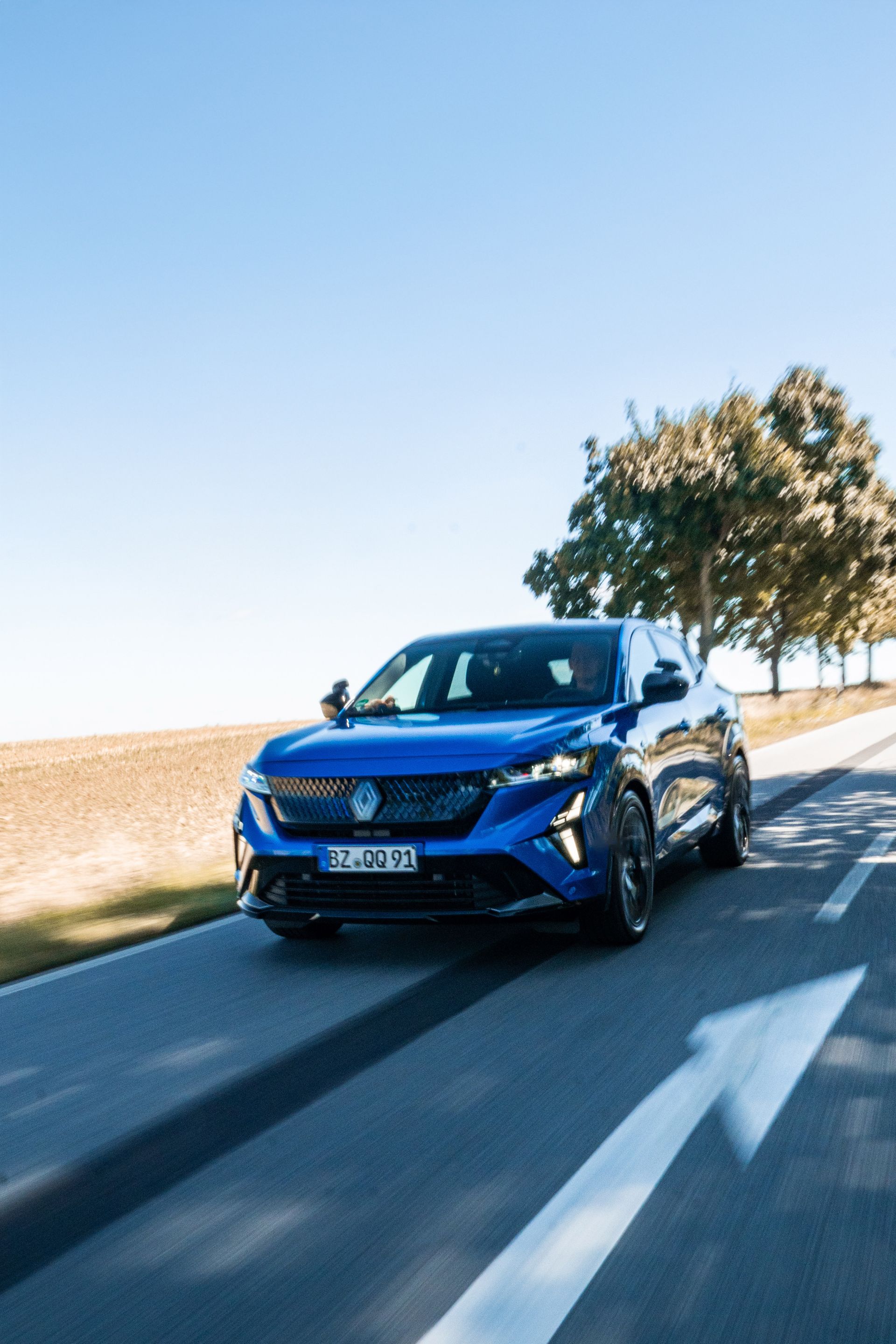 Blauer SUV fährt auf einer Asphaltstraße, sonniger Tag.