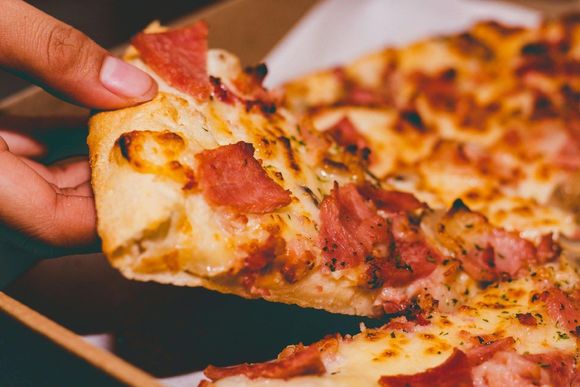 Rebanada de pizza con ingredientes, siendo recogida de una caja de pizza.