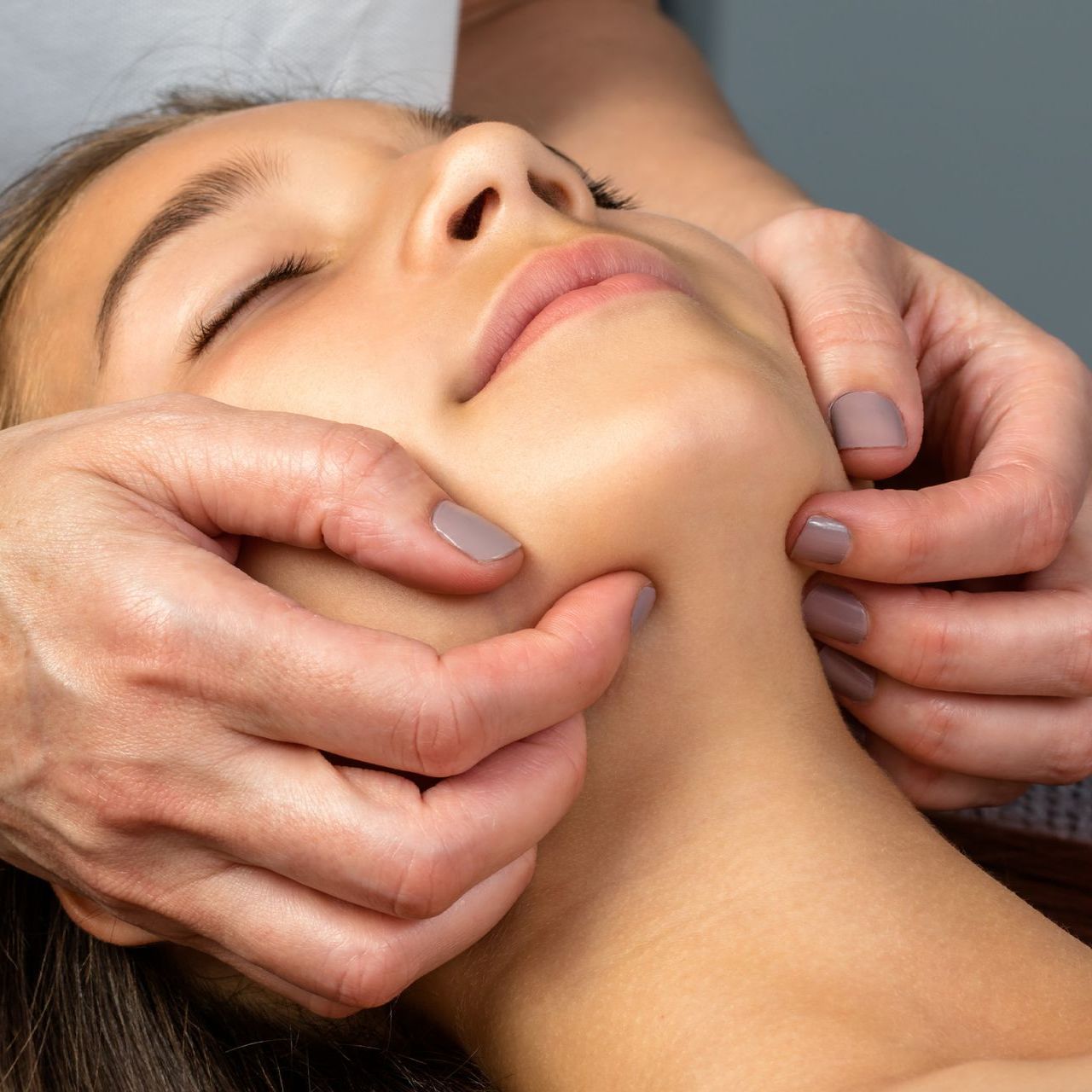Una mujer está recibiendo un masaje facial con los ojos cerrados.