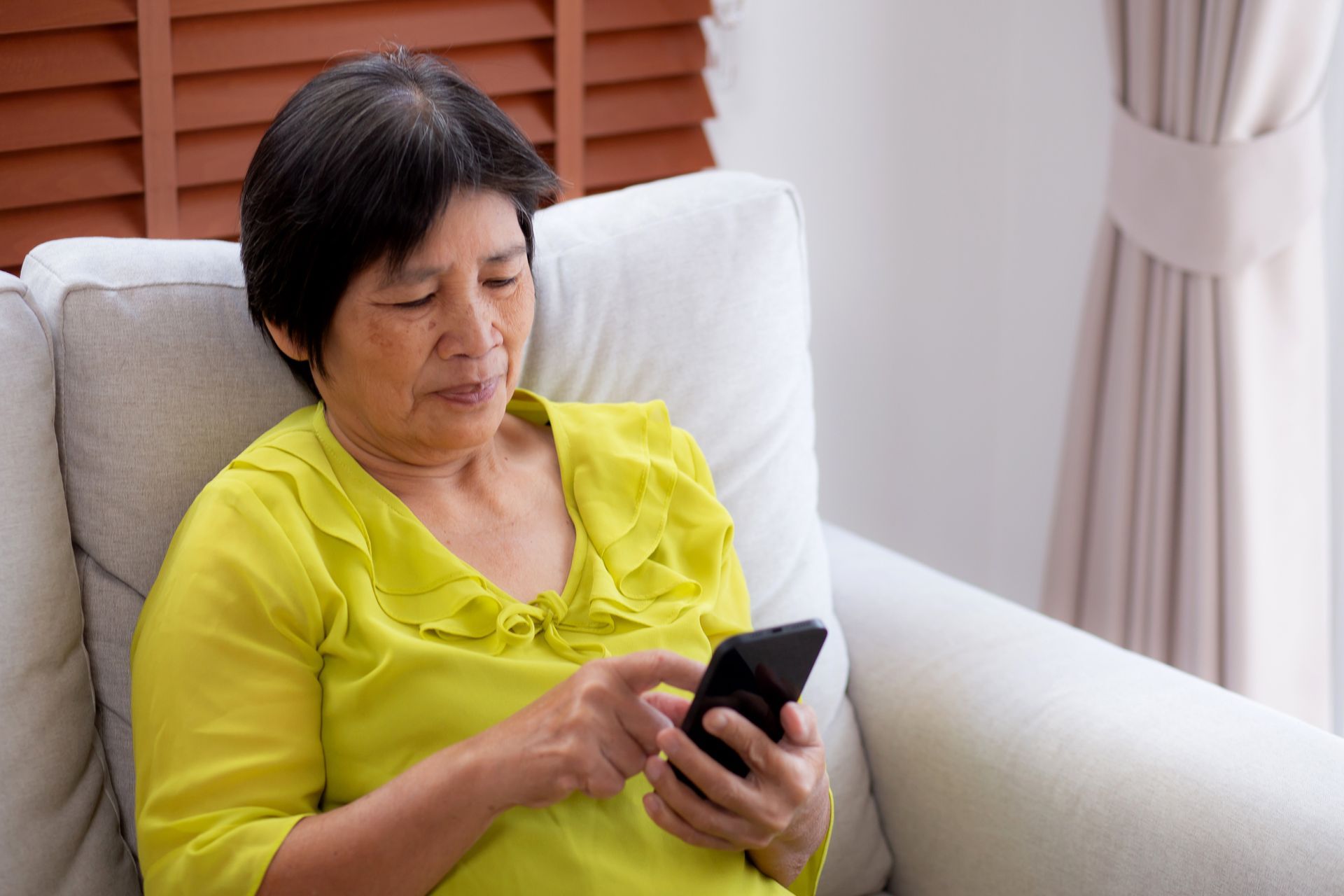 Une femme âgée, assise sur son canapé, regarde son téléphone