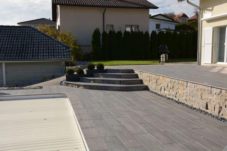 Terrasse avec marches en pierre, mur de soutènement et cour arrière avec une maison.