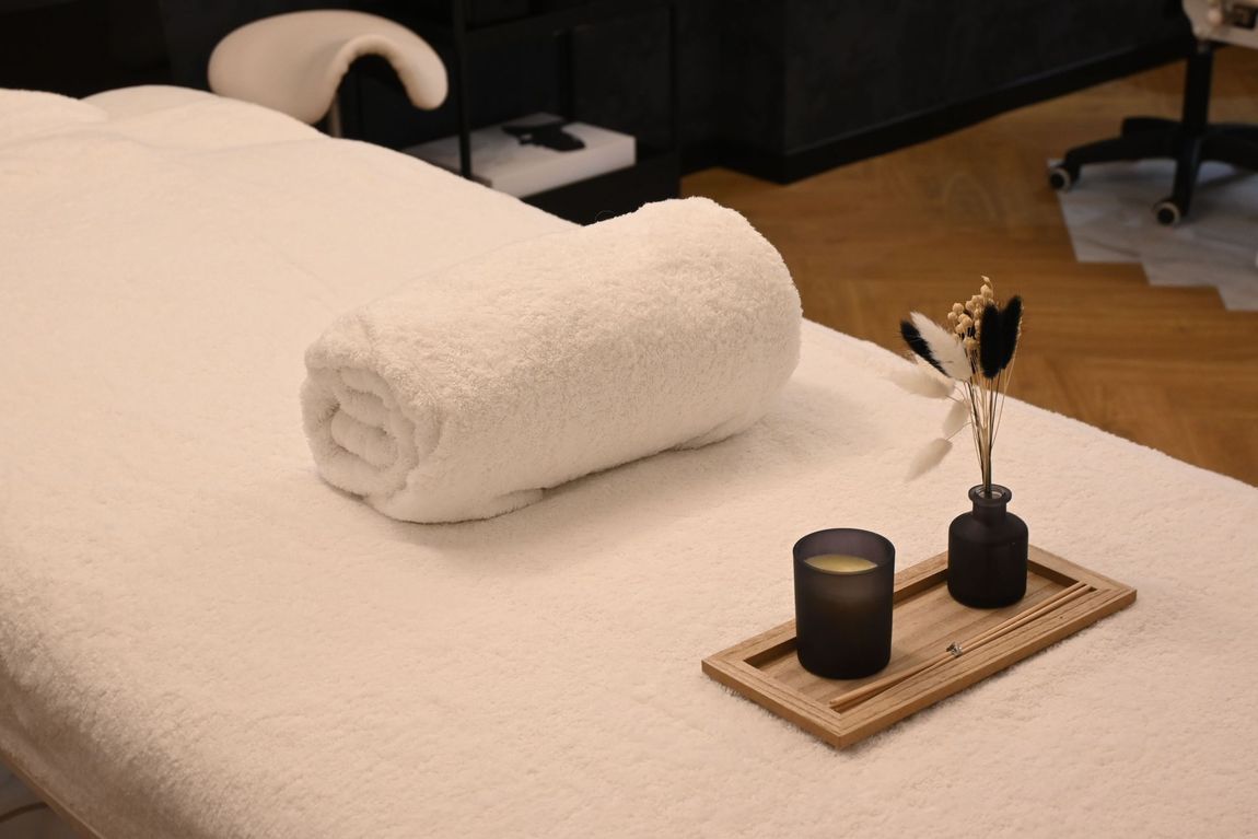 Salle de spa minimaliste avec table de massage blanche, serviettes pliées, paravent en bambou et petit décor en bois.