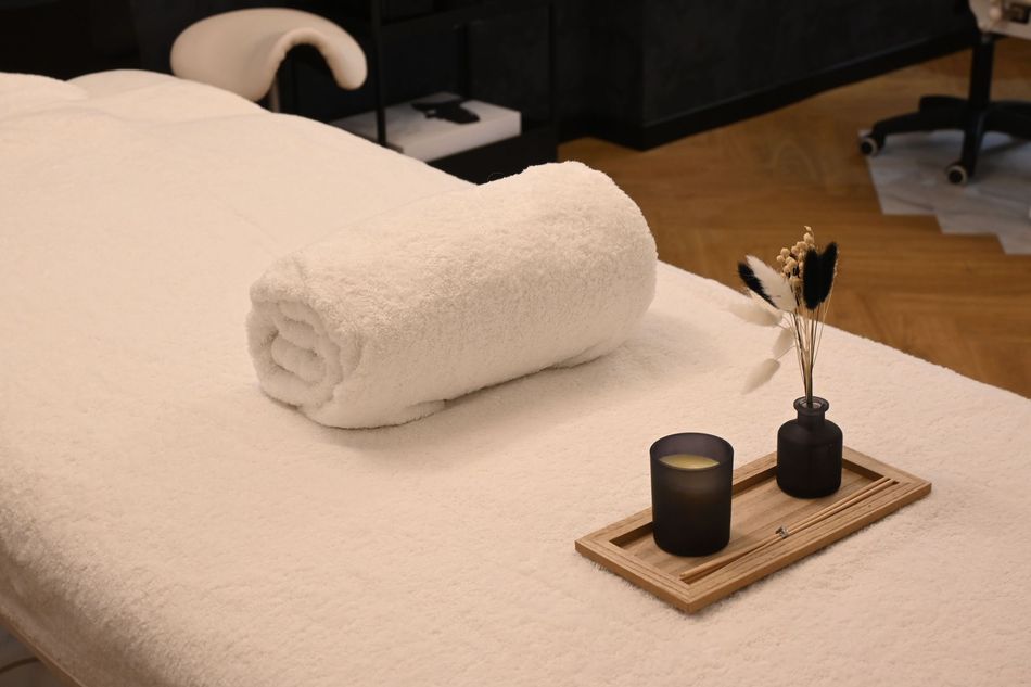 Salle de spa minimaliste avec table de massage blanche, serviettes pliées, paravent en bambou et petit décor en bois.