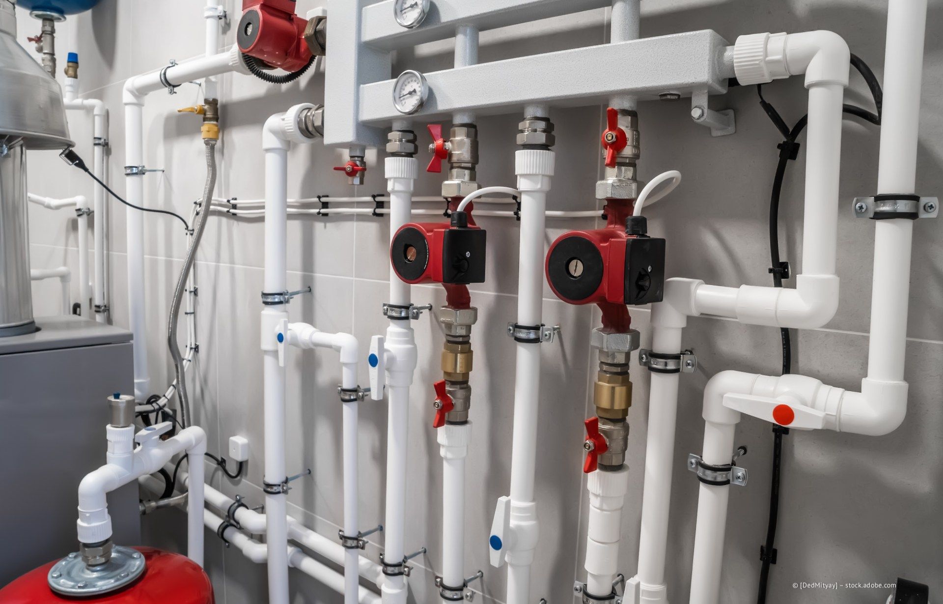 Industrieller Heizraum mit roten Pumpen und weißen Rohren an einer grauen Wand