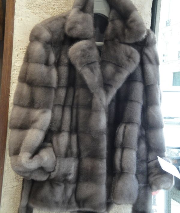 Un manteau de fourrure grise est exposé, avec un large col et des poignets en peluche.