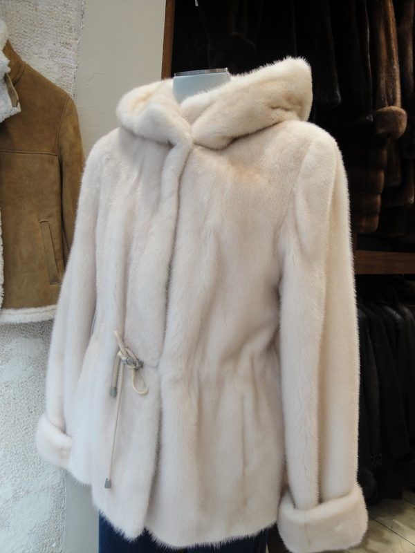 Manteau de fourrure blanc à capuche et ceinture, suspendu à un présentoir.