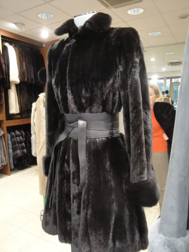 Manteau en fausse fourrure noire avec ceinture exposé dans un rayon de magasin de vêtements.