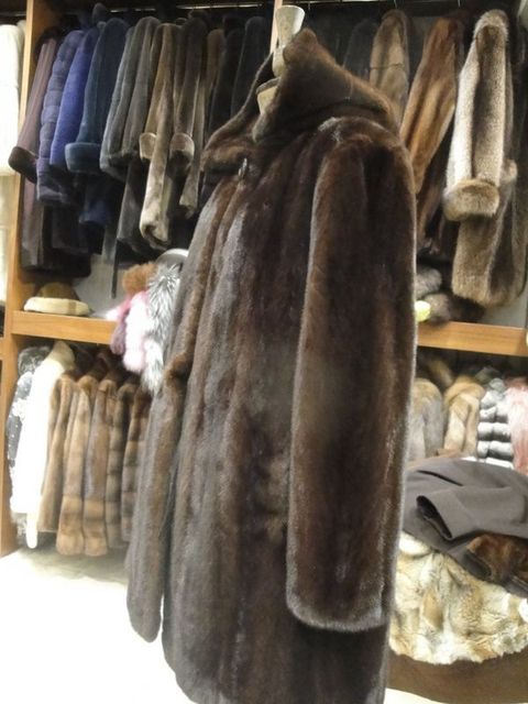 Des manteaux de fourrure suspendus à des portants dans un magasin de vêtements, avec un long manteau marron au premier plan.