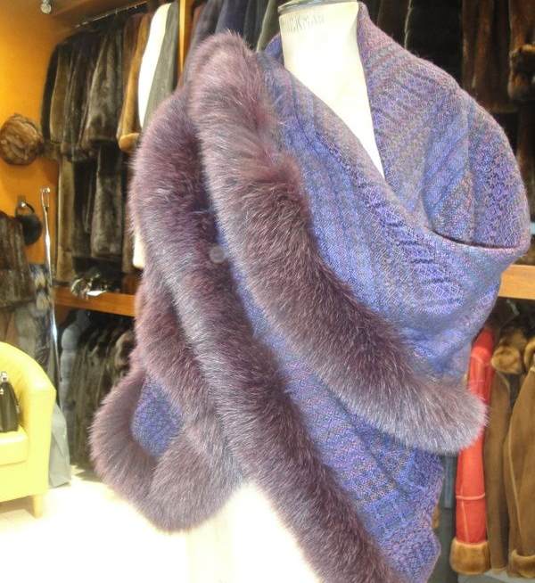 Un châle violet bordé de fourrure drapé sur un mannequin dans une boutique, avec des vestes suspendues derrière.