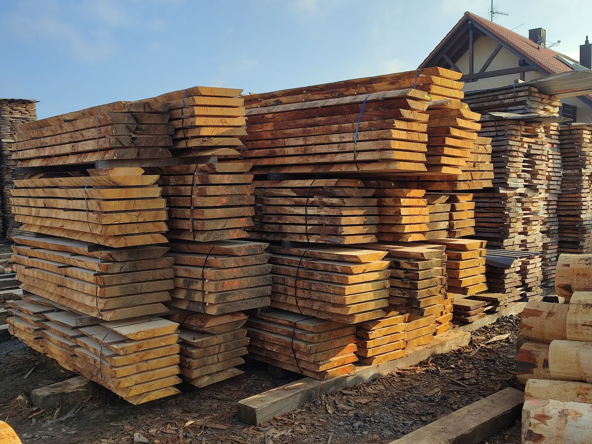Stapel verwitterter Holzbretter, draußen auf einem Holzplatz, unter blauem Himmel.
