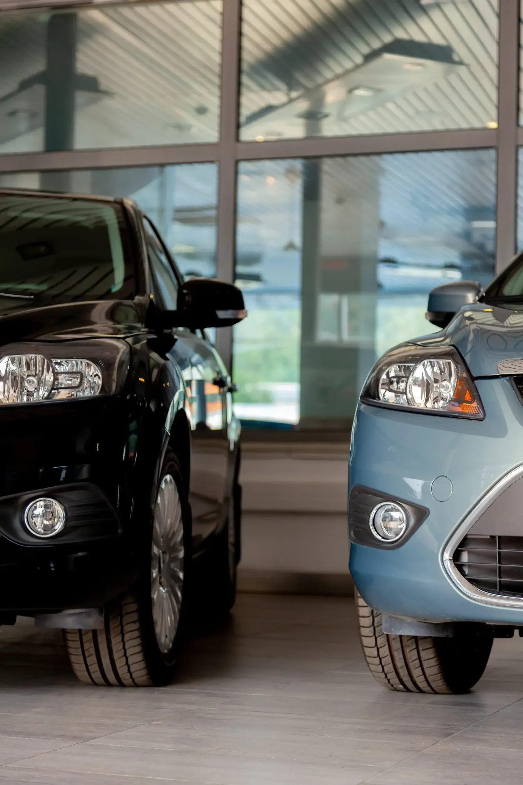 Vista frontal de un SUV negro y un sedán azul estacionados uno al lado del otro dentro de una sala de exposición.