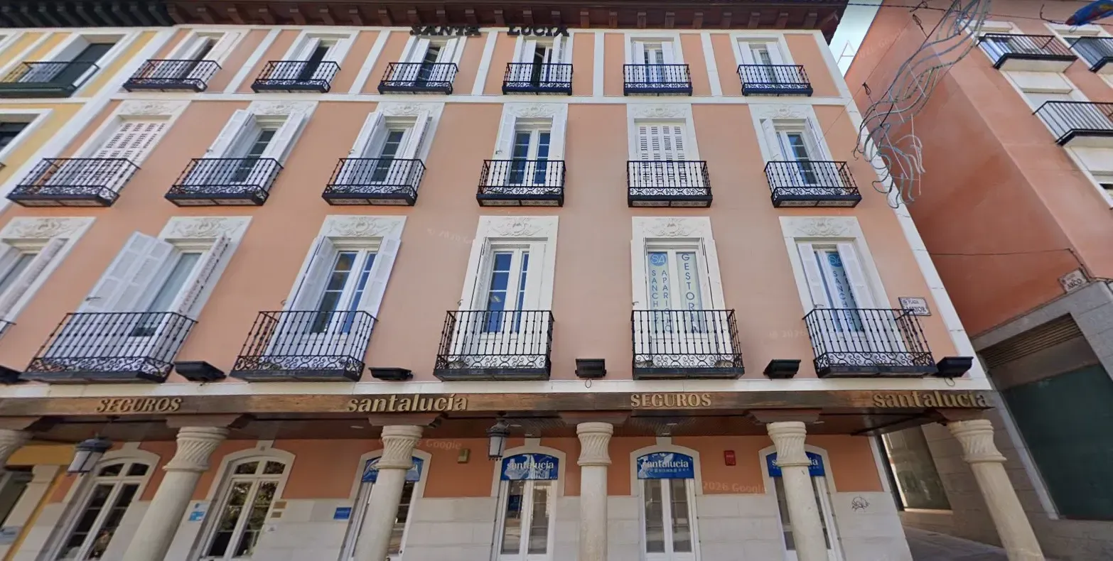 Una hilera de furgonetas de carga blancas idénticas aparcadas en fila al anochecer con los faros encendidos.