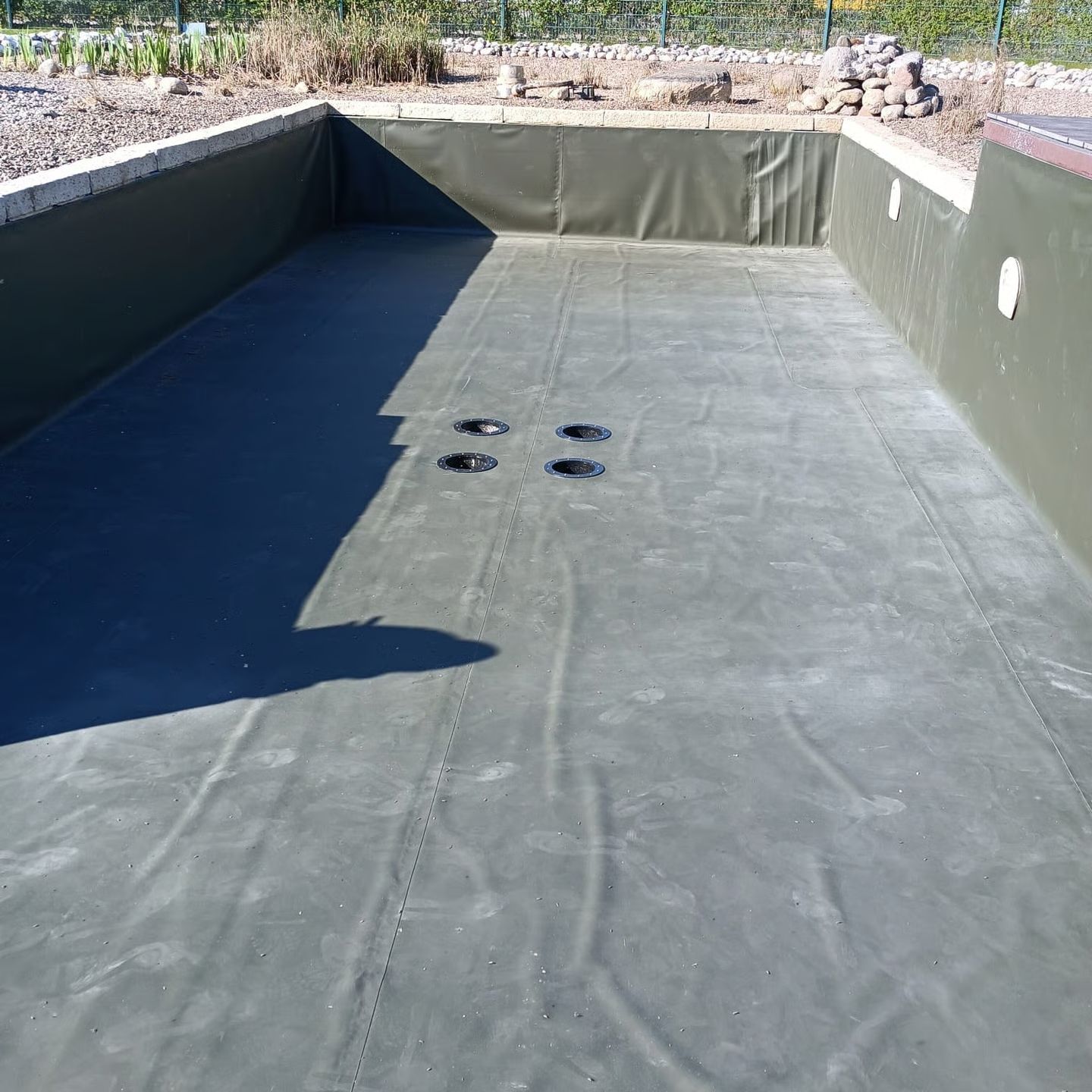 Ein rechteckiger, leerer Pool mit dunkelgrüner Auskleidung, der auf Wasser wartet.