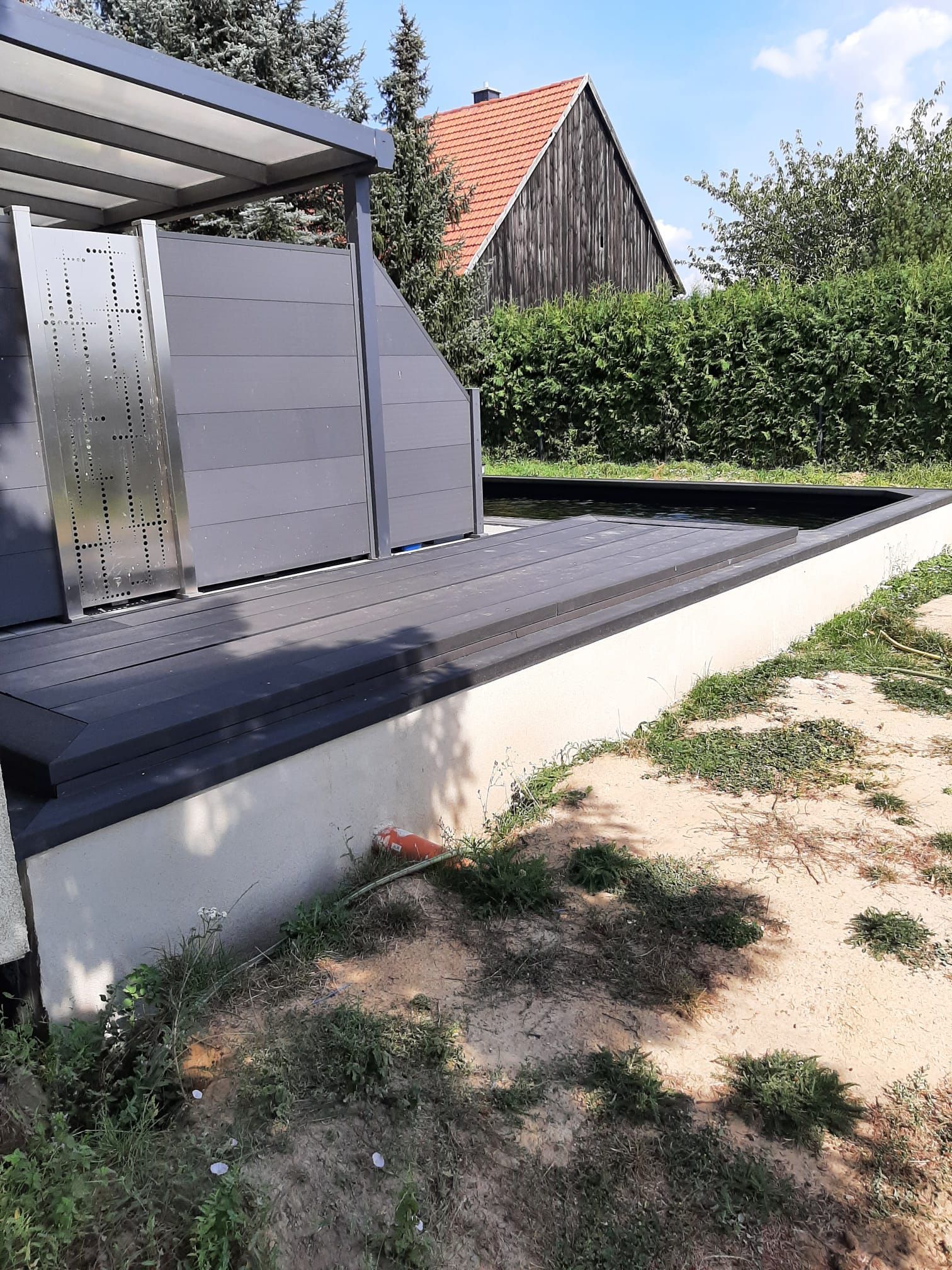 Außenterrasse mit dunkelgrauem Belag, niedriger weißer Mauer und grauer Pergola.