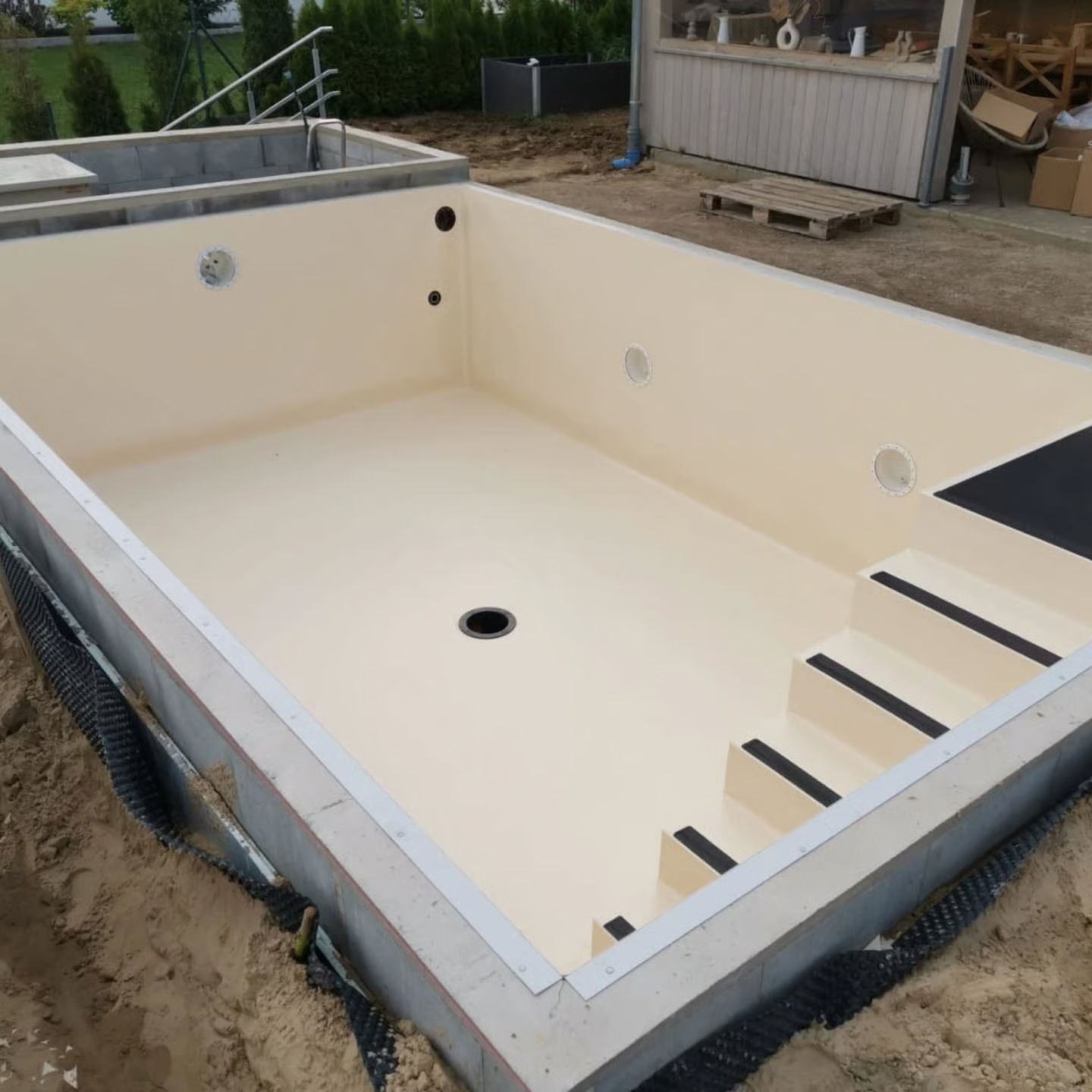 Unfertiger rechteckiger Pool mit Treppe und beigem Innenraum, umgeben von Beton und Erde.