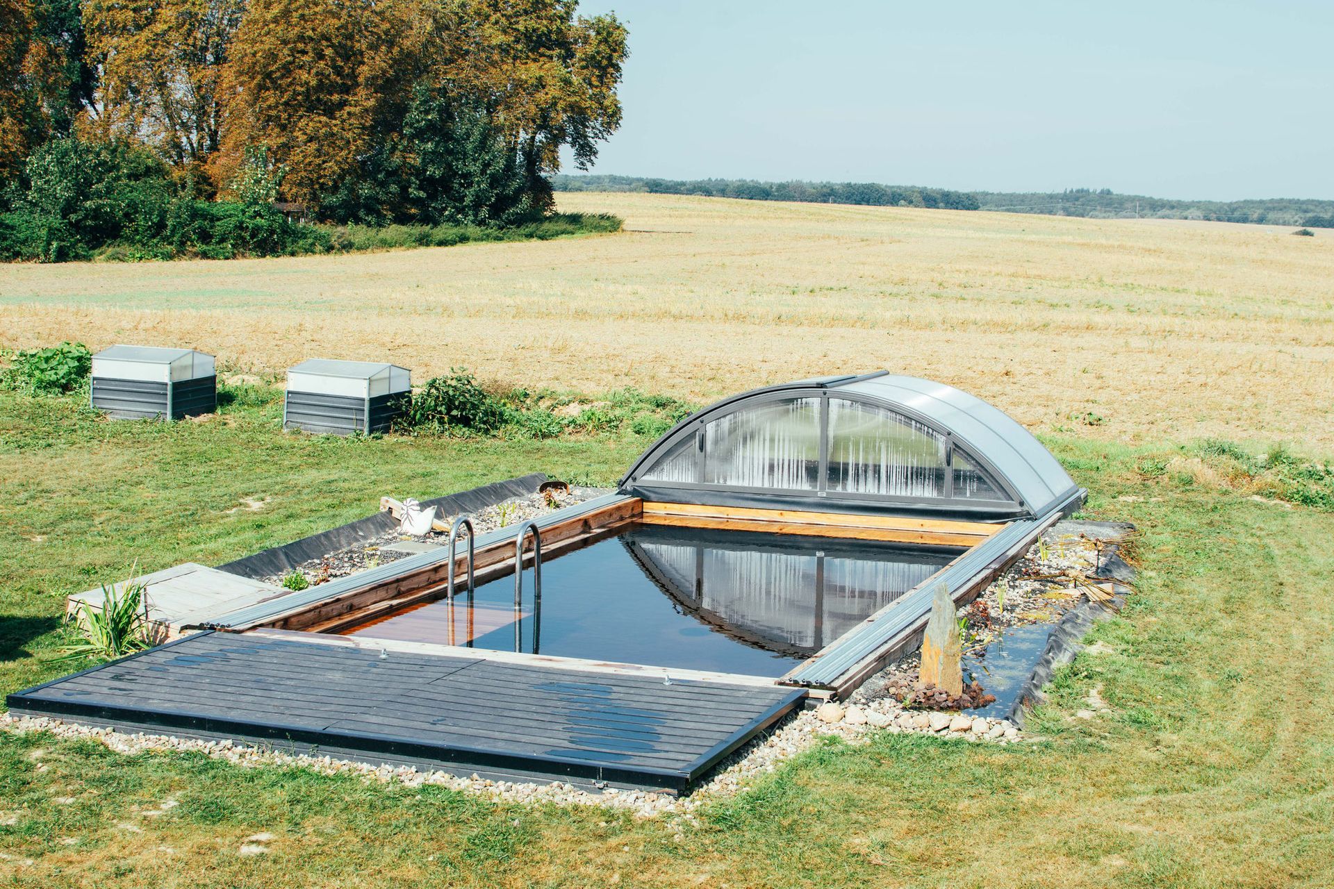 Rechteckiger Pool mit einziehbarer Abdeckung auf einer Wiese. Zwei kleine Schuppen in der Nähe.
