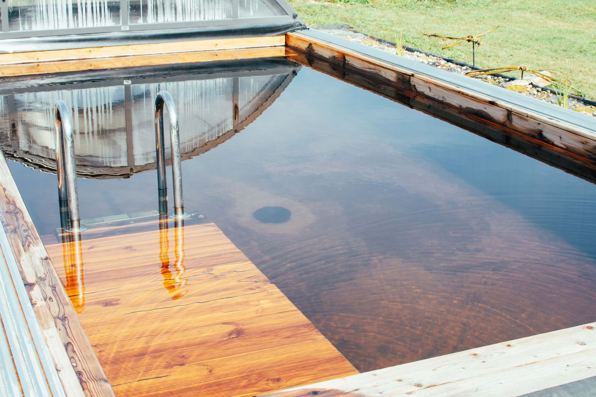 Hölzerner Außenpool mit Treppe und teilweise offener Abdeckung, mit Wasser gefüllt.