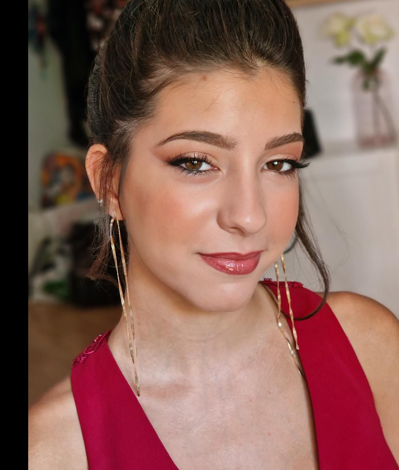 Mujer con el cabello recogido, blusa roja y largos pendientes dorados. Lleva maquillaje completo con sombra de ojos neutra