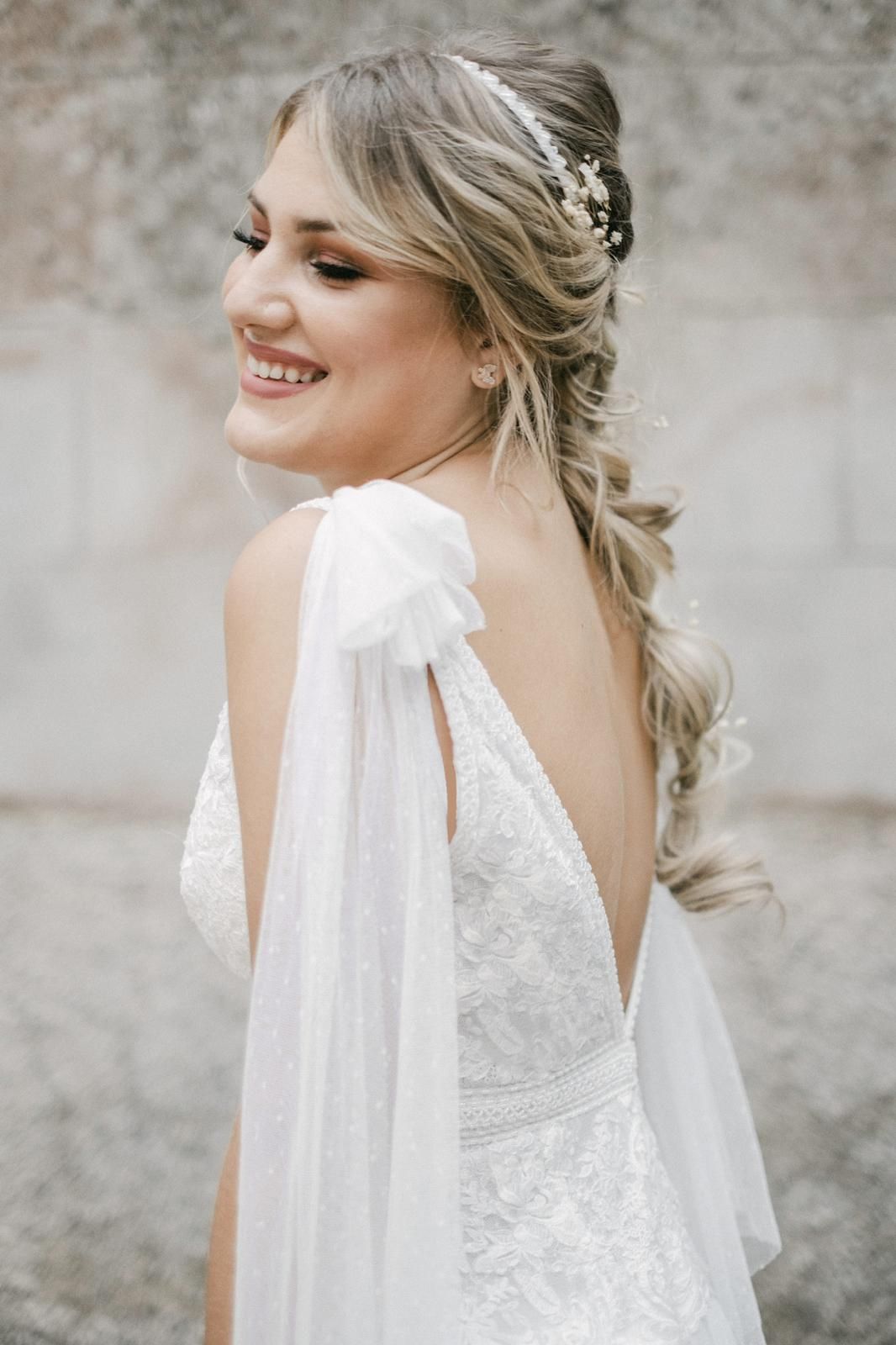 Novia con vestido blanco y trenza suelta sonríe, al aire libre.