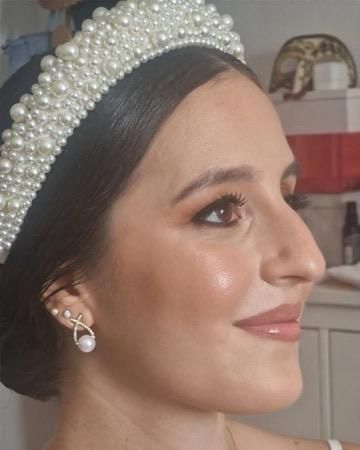 Mujer con tiara y pendientes de perlas, maquillaje marrón y una sonrisa sutil.