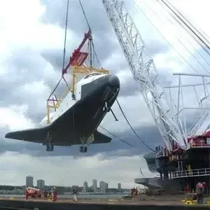 Ein Space Shuttle wird von einem Kran in die Luft gehoben.