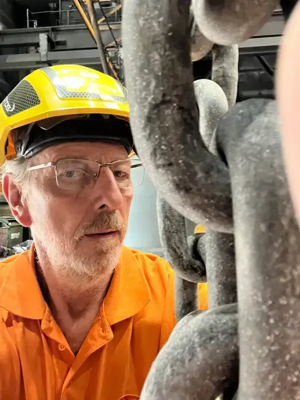 Ein Mann mit Schutzhelm und Brille betrachtet eine Kette.