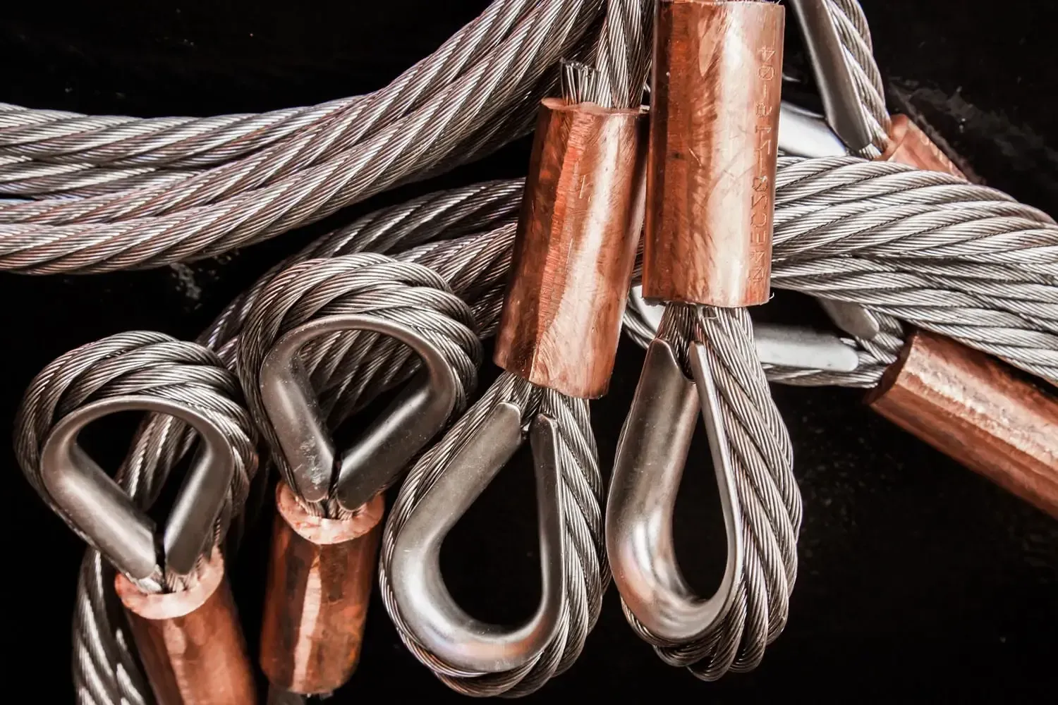 Ein Bündel Drahtseile mit Kupferhaken auf schwarzem Hintergrund.
