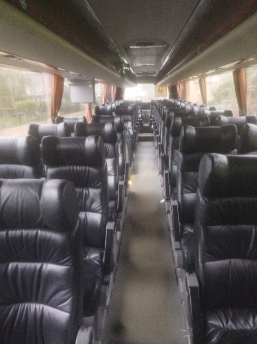 Interior dun autobús baleiro, con filas de asentos negros e grandes xanelas laterais