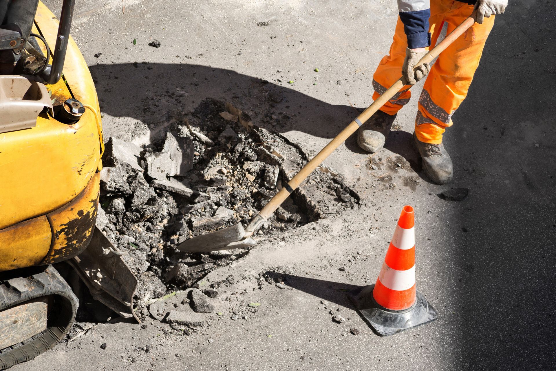 Ouvrier du bâtiment en pantalon orange et gilet de sécurité réparant une route.