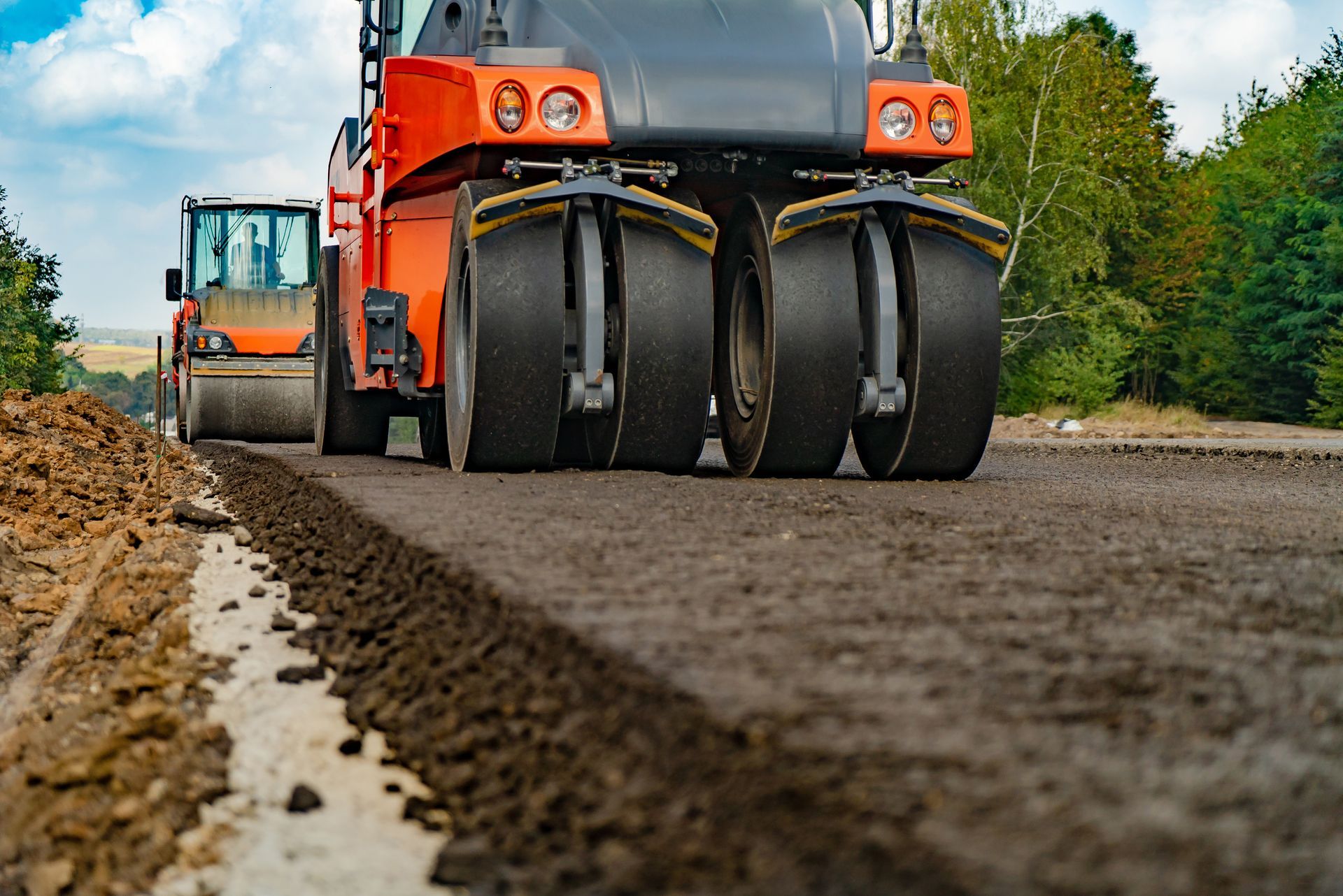 Rouleaux compresseurs compactant l'asphalte sur un chantier ; engins orange et jaunes.