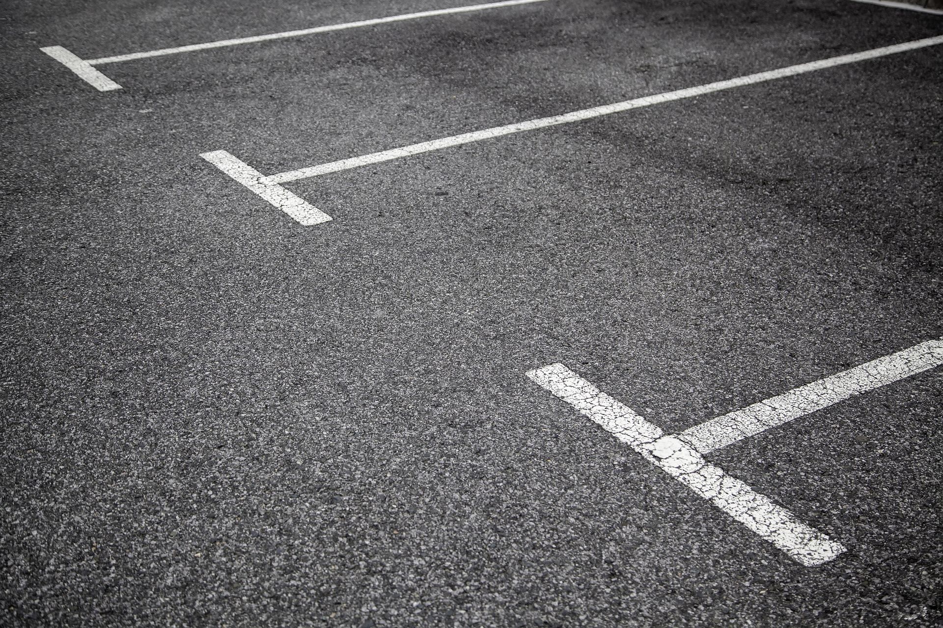 Marquages ​​de places de stationnement en asphalte ; lignes blanches sur surface gris foncé.