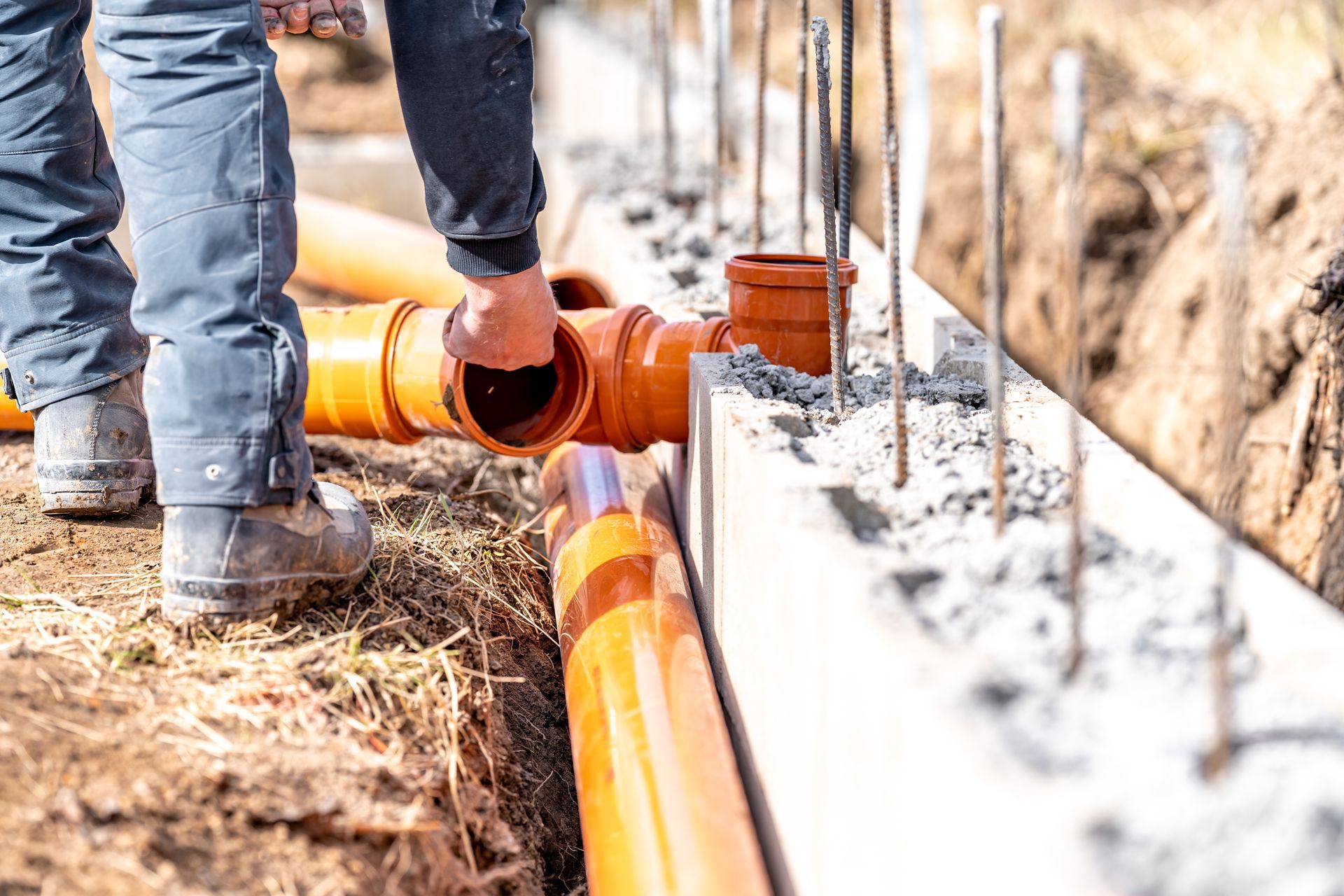 Un ouvrier du bâtiment installe des tuyaux de drainage orange près d'un mur en béton.