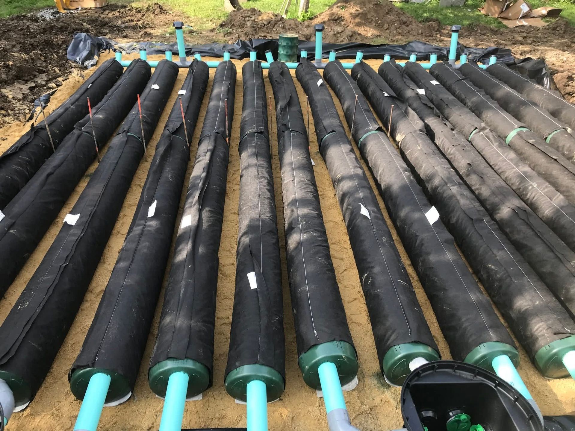 Des tubes noirs disposés en rangées, reliés par des tuyaux bleus, sur un lit de matériau beige.