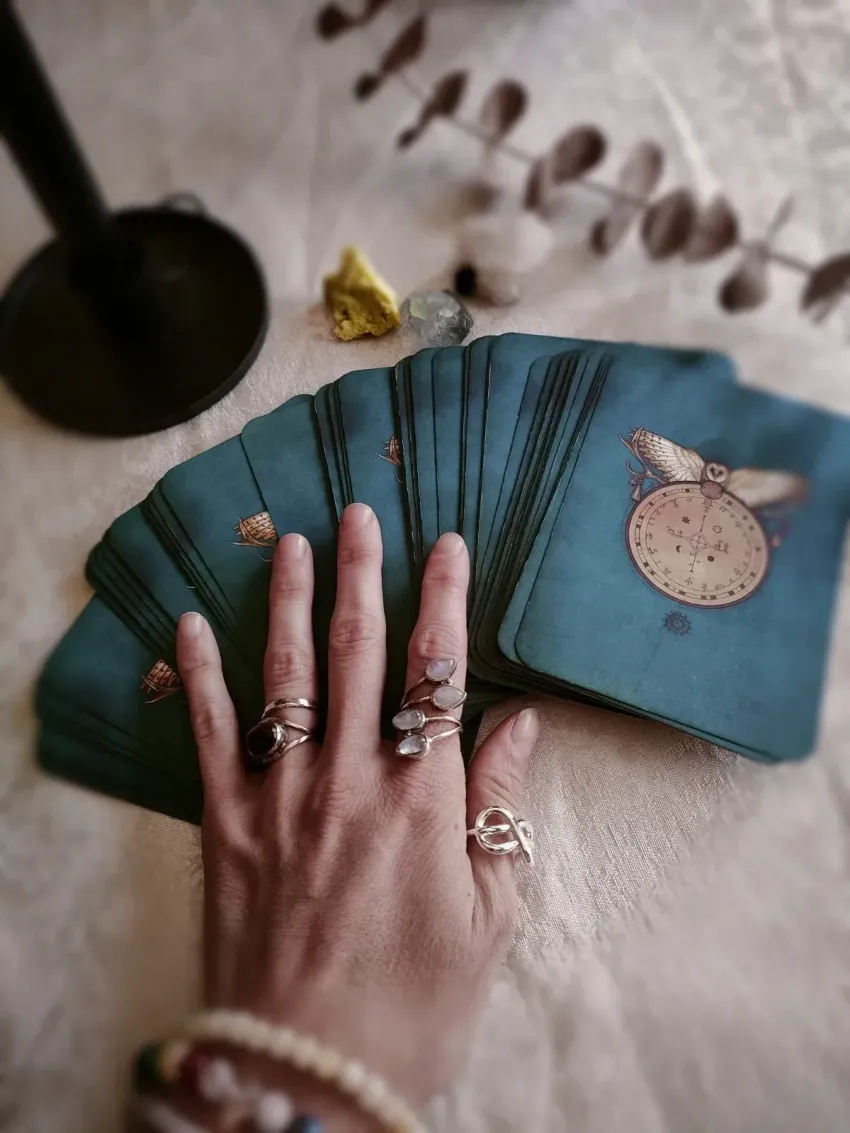 Una persona con anillos en sus dedos sostiene un abanico de cartas del tarot.