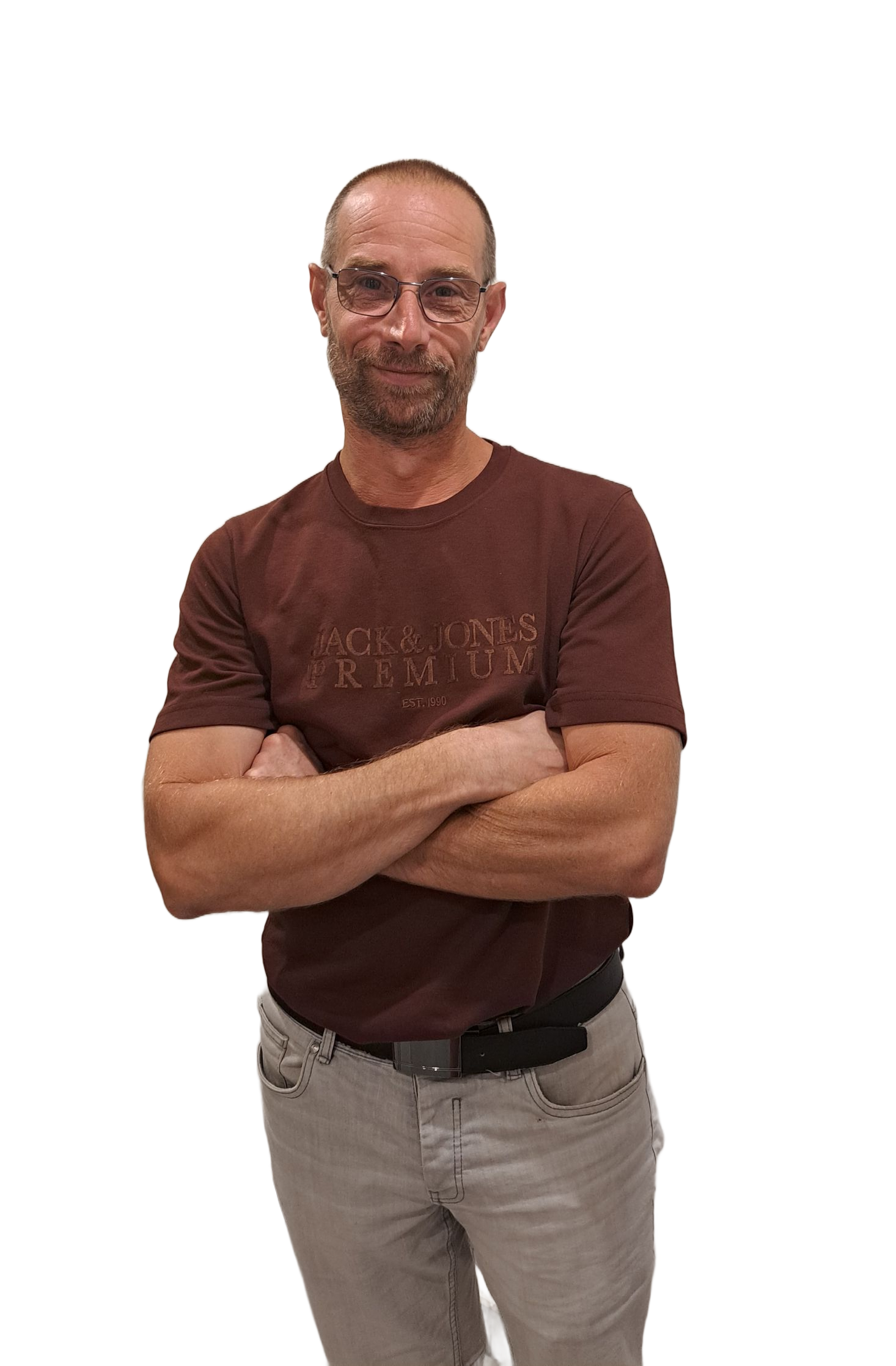 Un homme se tient debout sur fond blanc, vêtu d'un t-shirt et d'un pantalon beiges, regardant l'objectif.