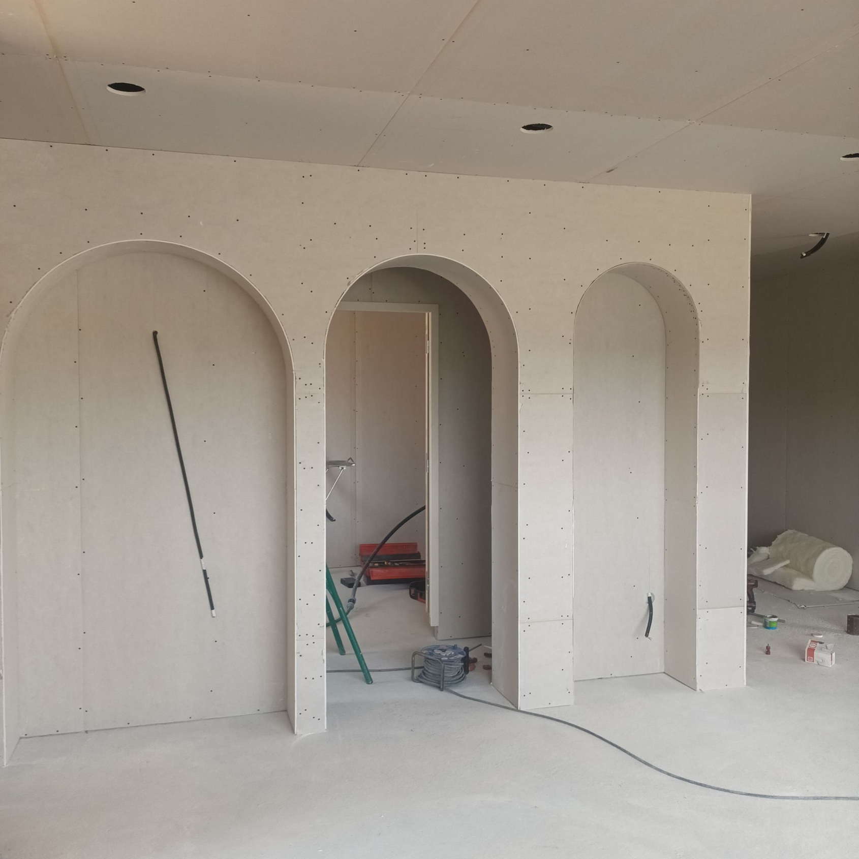 Pièce intérieure en construction avec trois niches murales cintrées blanches et des outils au sol.